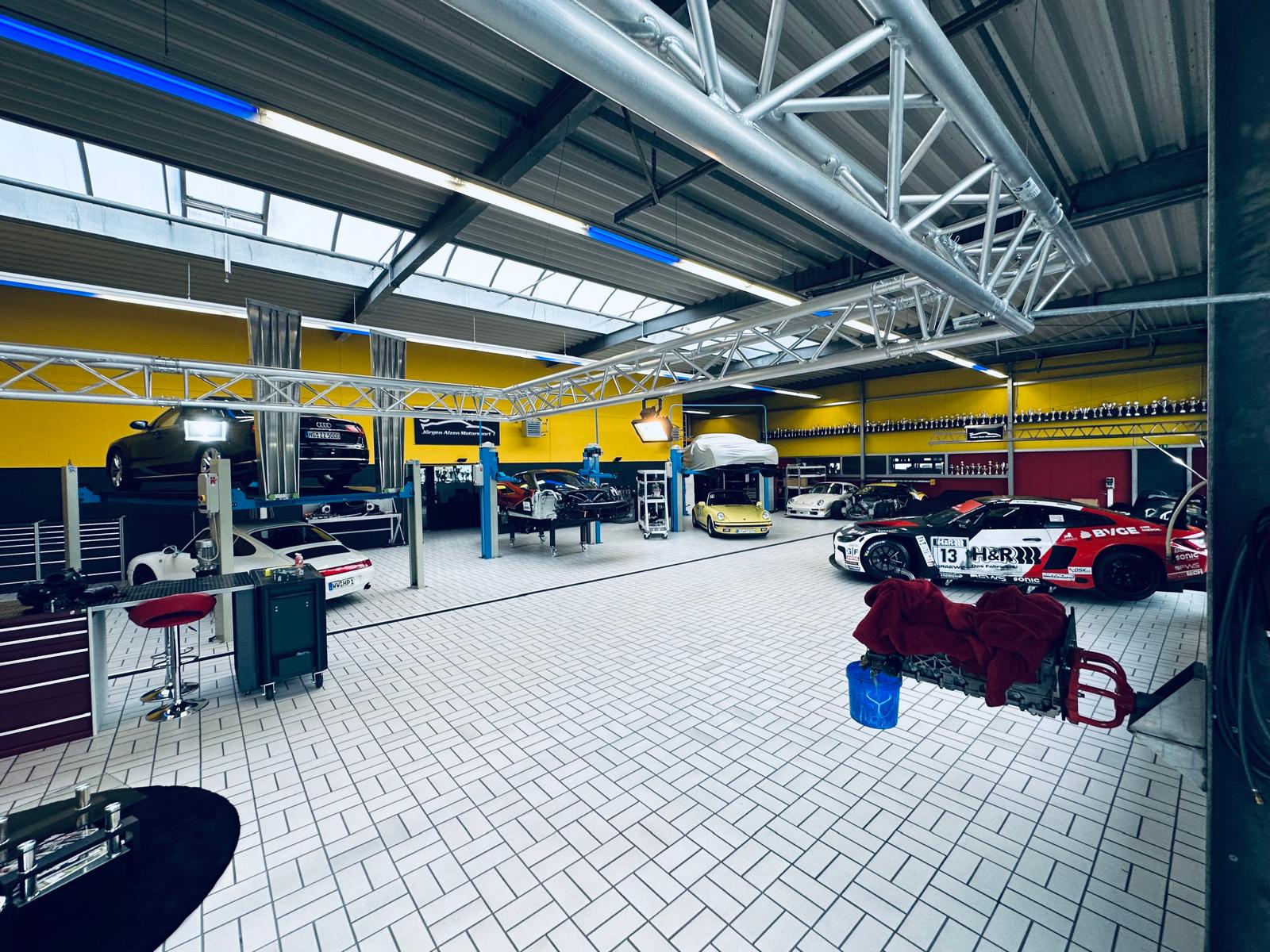 Geräumige Werkstatt mit verschiedenen Fahrzeugen, Werkzeugen und gelben Wänden.